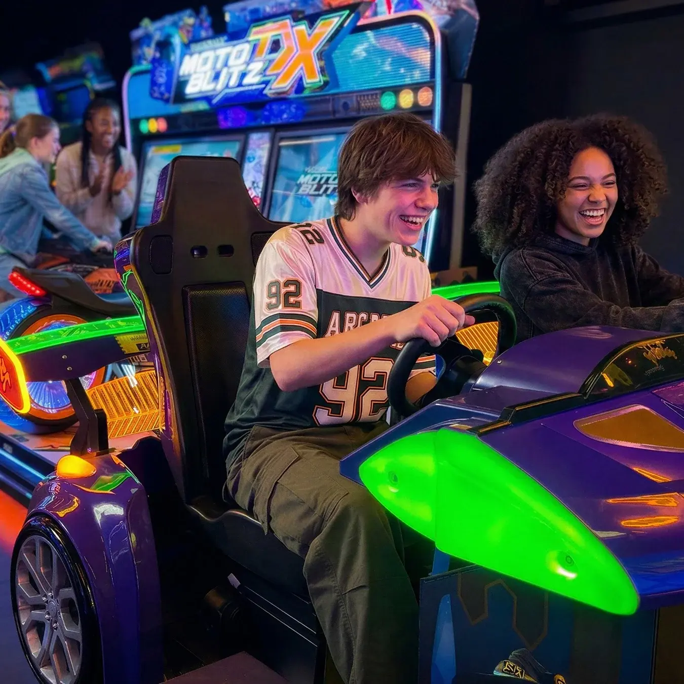 Deux jeunes joueurs hilares sur bornes de jeu de course en salle d'arcade en gare
